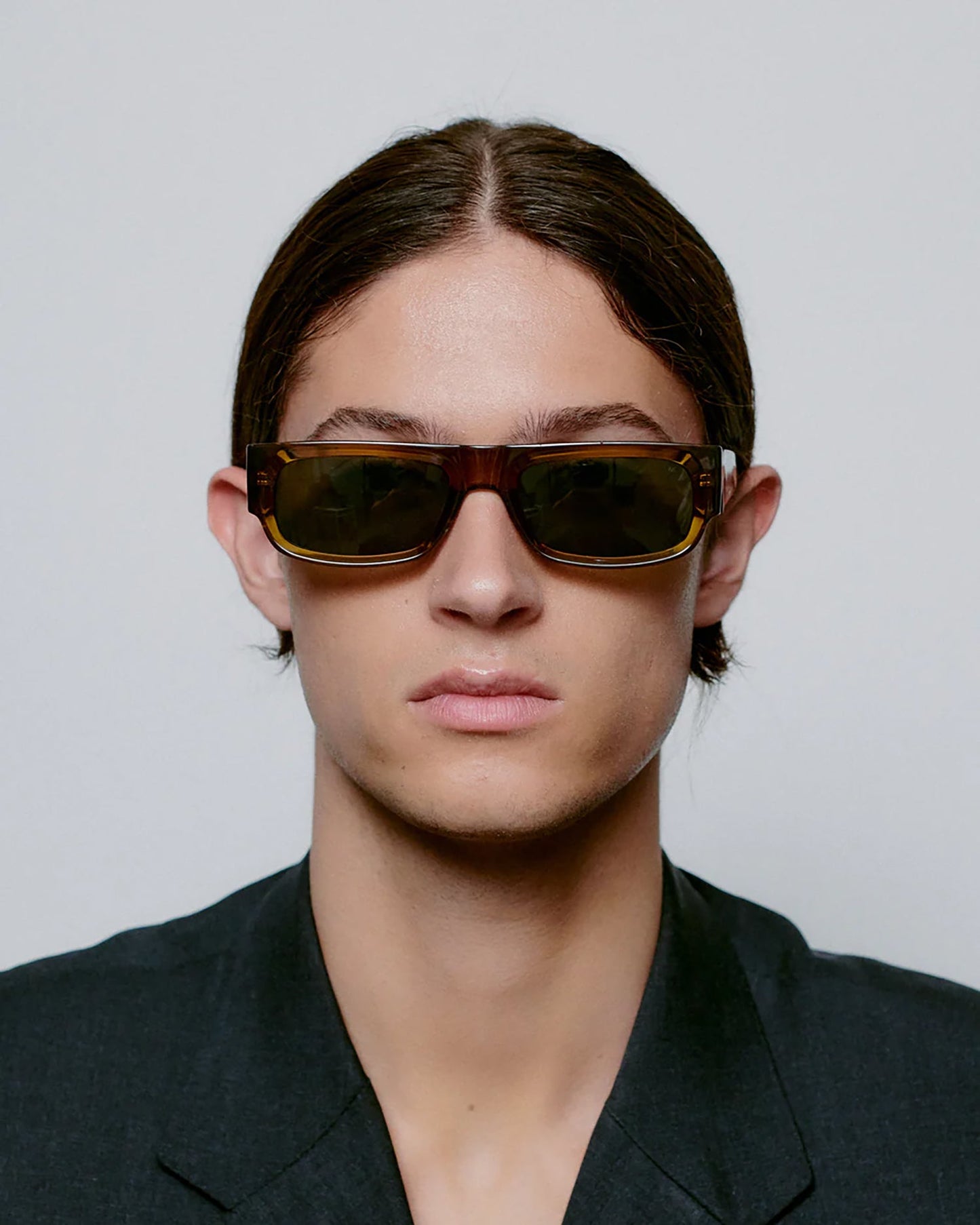 Person wearing dark sunglasses and a black outfit against a plain background