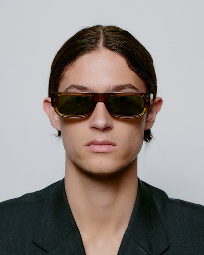 Person wearing dark sunglasses and a black outfit against a plain background