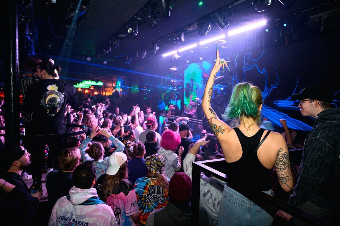 Person with green hair and tattoos at a concert, surrounded by a crowd in a dimly lit venue.